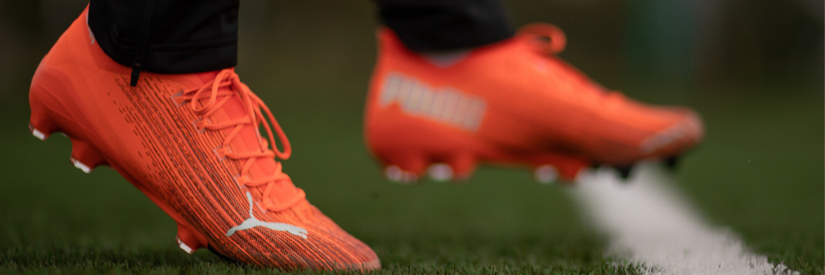 Football player wears firm ground football boots on dry, hard pitch