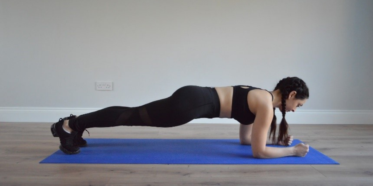 fitness model performing plank position working out at home on yoga mat